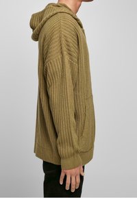 Khaki prążkowana dzianinowa bluza z kapturem ze sznurkiem, przednią kieszenią i luźnym krojem. Charakteryzuje się fakturowaną tkaniną oraz lekko zaokrąglonym dołem.