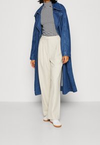 Dżinsowy długi płaszcz, paskowany golf, jasnobeżowe szerokie spodnie i białe trampki z gumową podeszwą. Casualowy strój z warstwowymi teksturami.