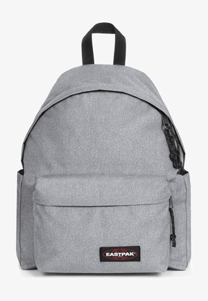 Sac à dos en tissu gris avec un dessus arrondi, une poche avant, des accessoires noirs et une poignée supérieure. Il présente une surface texturée et une patch logo.