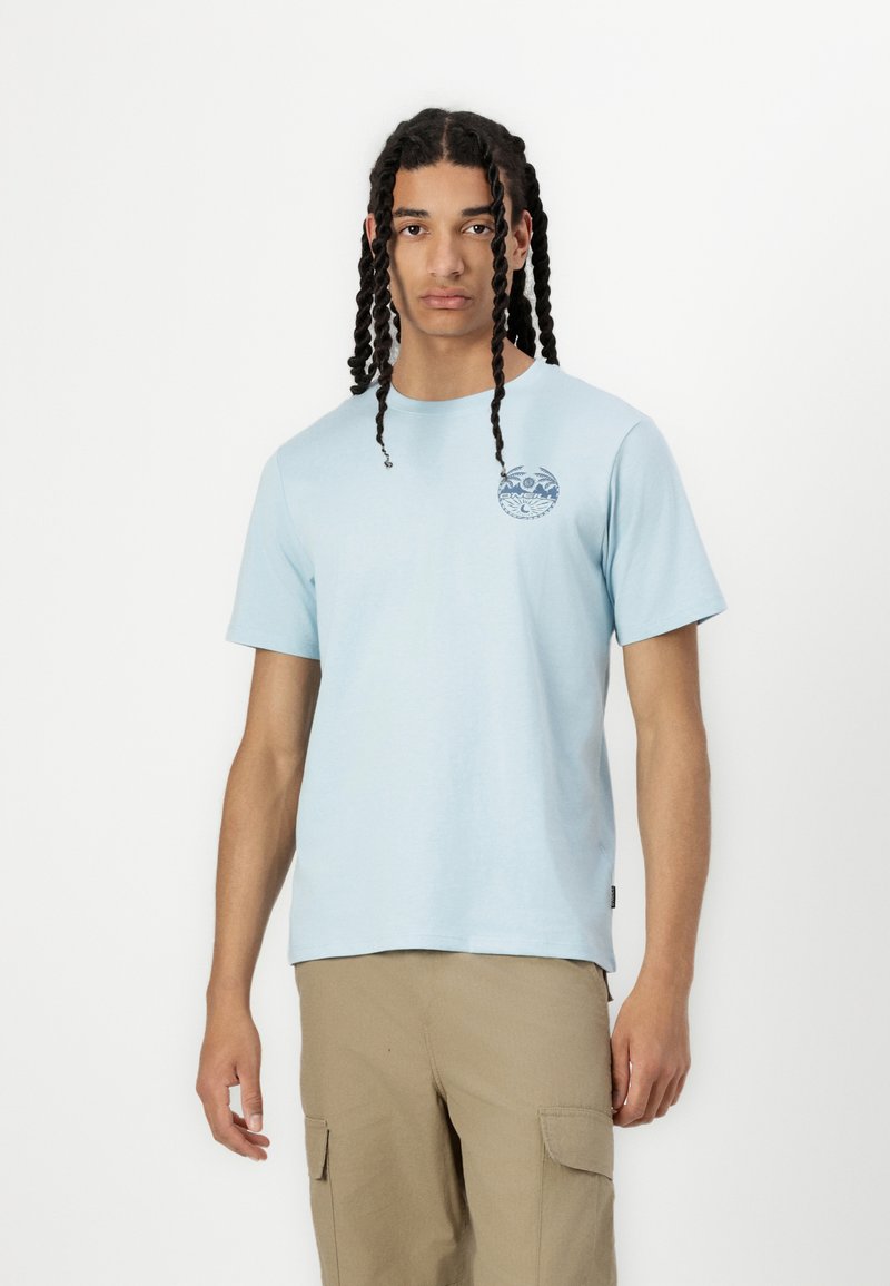 Tricou din bumbac de culoare albastru deschis, cu guler rotund, mâneci scurte și un design grafic circular pe partea stângă a pieptului.