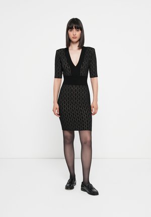 Svart bodycon-kjole med korte ermer, dyp V-hals, strukturert mønster og tettsittende midje. Bært med gjennomsiktige svarte strømpebukser og svarte loafers.