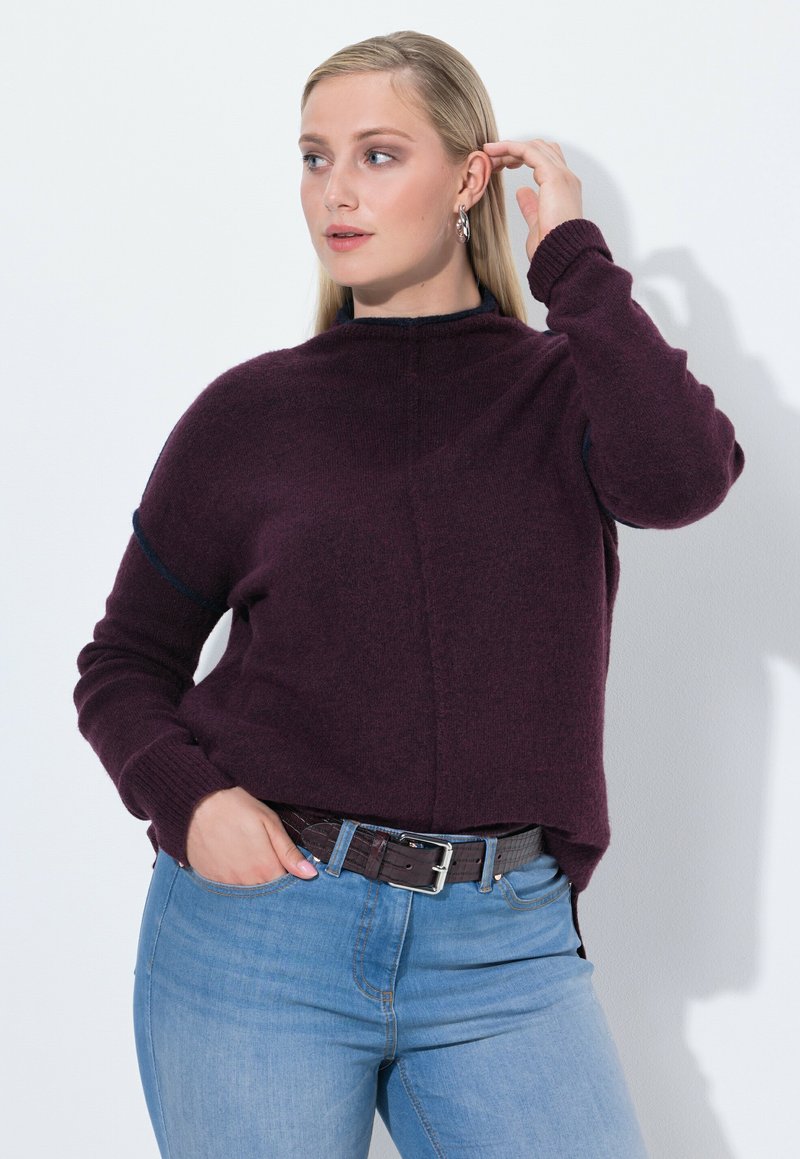 Burgundy strikket sweater med høj hals, ribbede manchetter og en afslappet pasform, parret med lyseblå jeans og et mørkebrunt bælte.