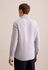 Camicia a maniche lunghe in lino grigio chiaro con vestibilità rilassata, polsini con bottoni e dettaglio della yoke posteriore. Tessuto leggero con un aspetto leggermente stropicciato.