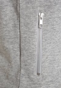 Tessuto di felpa grigia con una zip argentata visibile sul lato. La texture è morbida e presenta un sottile motivo melangiato.