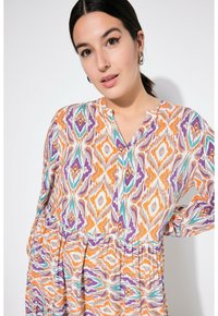 Multikleurige tuniek met oranje, paarse en teal geometrische patronen. Zacht stof, v-hals, losse pasvorm en geplooide taille detail.