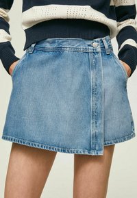 Denimkjol i ljusblått, med ett lagerdesign, framfickor och rå fåll. Materialet är mjukt med en något sliten struktur.