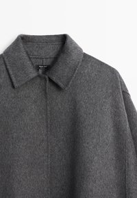 Manteau en laine grise avec un col classique, présentant un tissu texturé et un design épuré. Aucun système de fermeture ni motif visible.