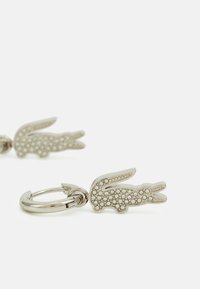 Portachiavi a forma di coniglio argentato con superficie texturizzata e cristalli trasparenti. Il design è semplice e moderno, attaccato a un anello metallico.