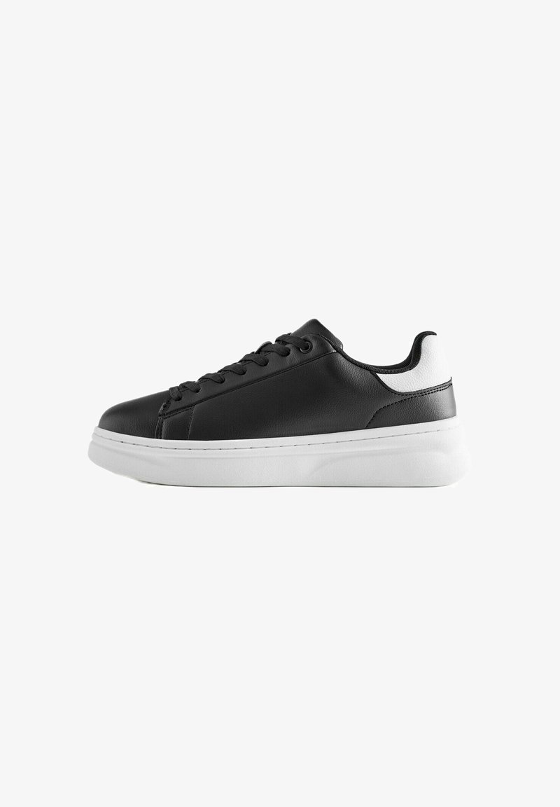 Baskets basses noires avec talon blanc et semelle blanche épaisse, avec des lacets noirs et une tige en cuir lisse.
