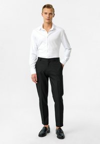 Witte blouse met lange mouwen, gecombineerd met zwarte op maat gemaakte broek en zwarte loafers. Glad stof en slim-fit ontwerp.