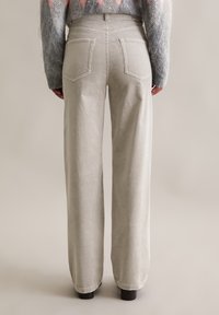 Hellgraue Cordhosen mit weitem Bein und vertikalen Rillen, ausgestattet mit zwei Gesäßtaschen und einem sauberen Saum. Weiche Textur und strukturierte Gestaltung.