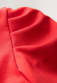 Rødt stof med en glat tekstur og let glans, der har folder og sømme, som skaber dybde og dimension.