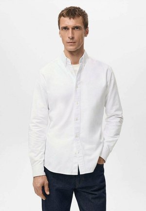 White button-up shirt made of cotton, featuring a collared neck, long sleeves, and a straight cut, displayed with dark denim pants.