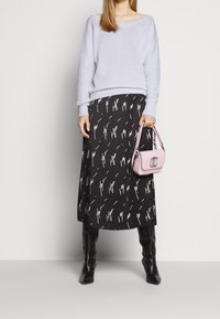 Maglione lavorato a maglia celeste, gonna nera plissettata con motivo astratto bianco, stivali neri al ginocchio e una piccola borsa rosa.
