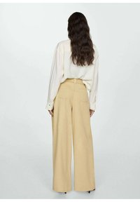 Beige wijde pantalons gemaakt van lichte stof, met achterzakken en een riem in de taille, gecombineerd met een losvallend off-white overhemd.