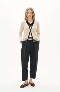 Gilet beige à côtes avec accents noirs, bouton devant et poignets rayés. Assorti à un pantalon plissé noir et des ballerines à imprimé léopard.