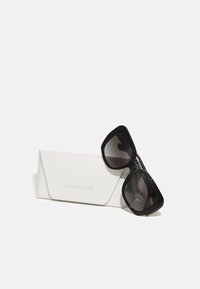 Gafas de sol negras de gran tamaño con lentes degradados, acompañadas de un estuche blanco texturizado con el logotipo en relieve "MICHAEL KORS".