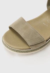 Beige semišové sandály s širokým páskem, měkkou stélkou a copánkovým detailem kolem lehké podrážky. Navrženo pro pohodlí a snadné nošení.