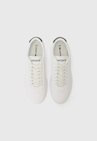 White leather sneakers featuring tonal laces, perforated detailing on the toe, and a black accent on the heel. Logo displayed on tongue.