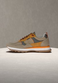 Αθλητικό παπούτσι casual σε μπεζ, καφέ και πορτοκαλί με λευκή σόλα και εξωτερική σόλα από καουτσούκ, εμφανίζεται σε ανοιχτή επιφάνεια με ουδέτερο φόντο.