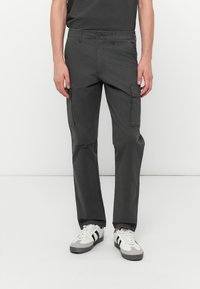 Pantaloni cargo gri cu croială dreaptă, dintr-un material durabil. Au buzunare laterale, curea și închidere cu nasture. Purtați cu adidași albi.