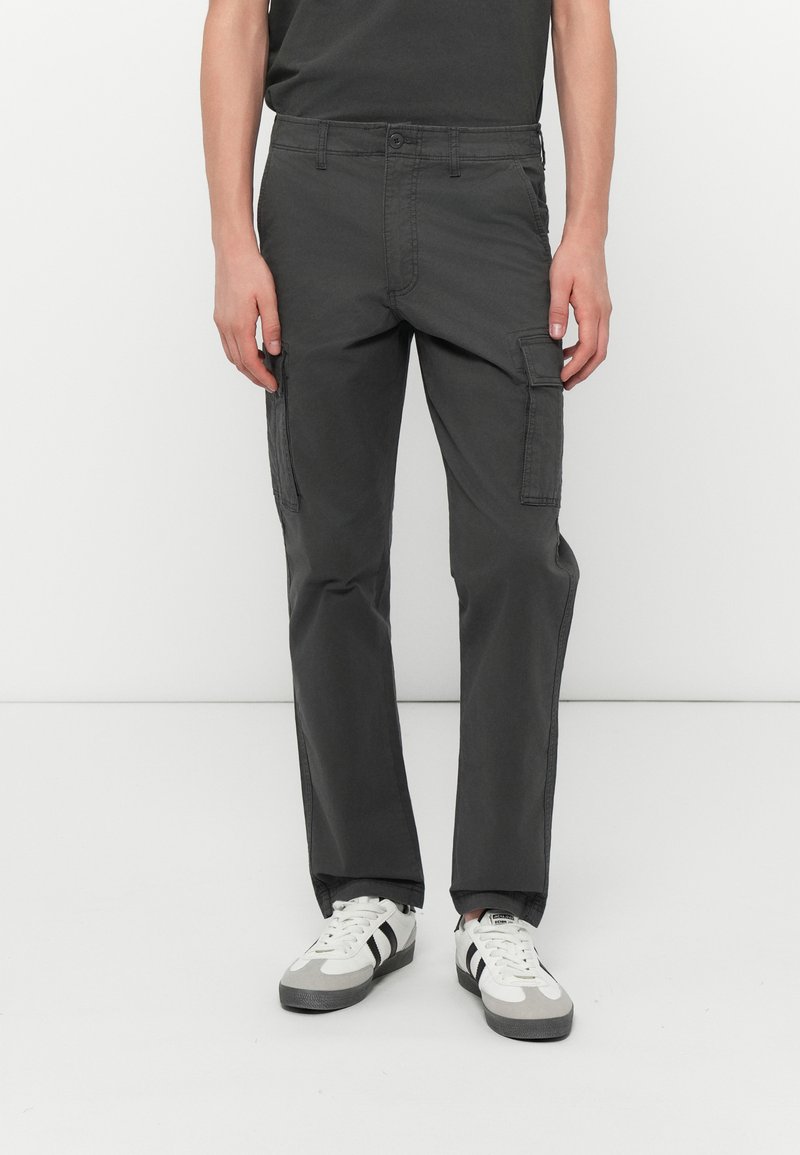 Pantaloni cargo gri cu croială dreaptă, dintr-un material durabil. Au buzunare laterale, curea și închidere cu nasture. Purtați cu adidași albi.
