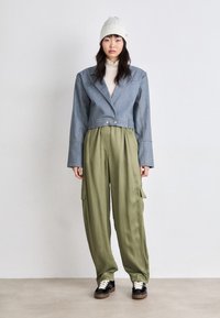 Cropped denim jacket with wide sleeves, olive green cargo pants with side pockets, and black sneakers with white laces and a brown sole.
