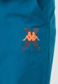 Teal athletic shorts featuring a pinstripe pattern. The left leg displays an orange logo with "X" and "FIT" beneath it, accented by two figures.
