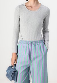 Light gray ribbed long-sleeve top paired with loose lavender pants featuring green stripes, held with a drawstring. A small blue handbag is included.