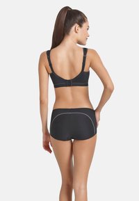 Zwarte sportbh met verstelbare bandjes en haaksluiting; gecombineerd met zwarte high-waisted shorts met contrasterende stiksels en mesh-details.