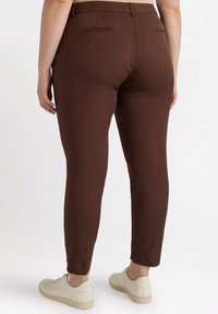 Pantaloni marroni aderenti con una texture liscia, taglio slim e due tasche posteriori. Abbinati a sneaker bianche.