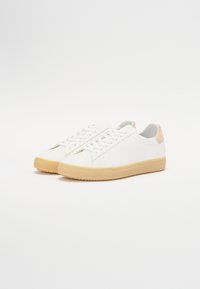 White sneakers with a smooth leather upper, round toe, and beige rubber outsole. Features lace-up closure and a contrasting heel accent.