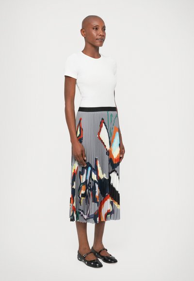 Fustă plissetată gri cu un model abstract colorat, asortată cu o cămașă albă ajustată și pantofi negri cu talpă joasă, cu accente decorative.