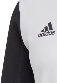 Koszulka Adidas z białym korpusem i czarnymi rękawami. Gładka tekstura, logo nadrukowane na klatce piersiowej w kolorze czarnym. Standardowy krój sportowy.