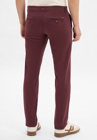 Chino bourgogne avec une coupe slim, comportant deux poches arrière avec boutons, des passants de ceinture et une texture lisse. Associé à des baskets blanches.