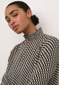 Sort og beige mønstret bluse med en høj, flæset krave og lange ærmer, prydet med et geometrisk design af skiftende former.