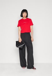 Red cotton t-shirt with white logo, high-waisted black wide-leg trousers, and a small black handbag, paired with multi-colored sandals.