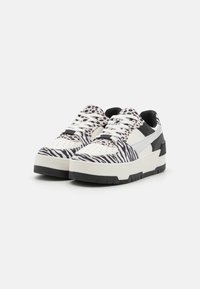Sapatilhas elegantes com um upper em padrão de zebra em preto e branco, apresentando uma sola espessa, detalhes brancos e atacadores pretos.