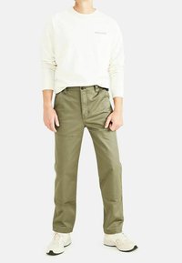 Olijfgroene katoenen broek met een rechte snit, voorzien van voorzakken en een knoopsluiting, gecombineerd met een witte sweatshirt en witte sneakers.