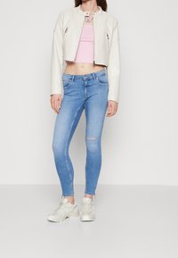Chaqueta corta de cuero crema, top corto ajustado rosa, jeans skinny azul claro con rotos en las rodillas y zapatillas gris claro.