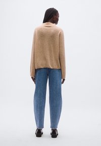 Beež tekstuuriga kootud kampsun, mis on lahtise lõikega, kombineeritud kõrge vöökohaga veidi kitsenevate siniste teksapükstega ja tumedate jalanõudega. Lihtne, ühtne komplekt.