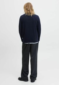 Suéter azul marino con cuello redondo, mangas largas y un corte holgado. Lleva puesto sobre una camisa de rayas clara y se combina con pantalones oscuros.