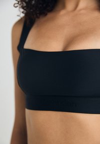 Svart BH med firkantet utringning og brede stropper. Har en jevn tekstur og en preget Calvin Klein-logo på båndet.