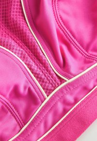 Felroze sportstof met een mesh-textuur, gladde delen en witte piping-accenten. Afwisselende afwerkingen creëren visuele interesse.