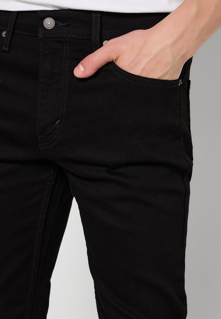 Pantaloni in denim nero con un design aderente, dotati di una tasca standard e dettagli in metallo argentato. Tessuto testurizzato con cuciture visibili.