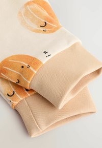 Manchettes de sweat en coton avec des motifs circulaires oranges sur une base crème, dotées d'une texture côtelée beige unie aux extrémités.