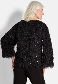 Zwarte gebreide trui met lange, brede mouwen en franjes. Sprankelende pailletten die overal verspreid zijn, voegen visuele aantrekkingskracht toe.
