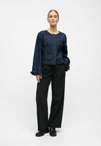 Jeansjacke mit langen, weiten Ärmeln und einem verkürzten Design, mit sichtbaren Nähten und Knopfdetails, kombiniert mit maßgeschneiderten schwarzen Hosen.