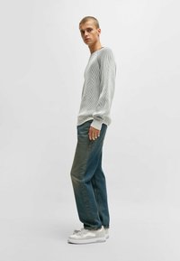 Long-sleeve, loose-fit light gray knit sweater with ribbed texture; paired with medium-wash straight-leg jeans and white sneakers.