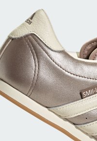 Metallic silver sneaker featuring soft beige accents, a textured leather upper, and a contrasting gum rubber sole. Notable stitching details present.